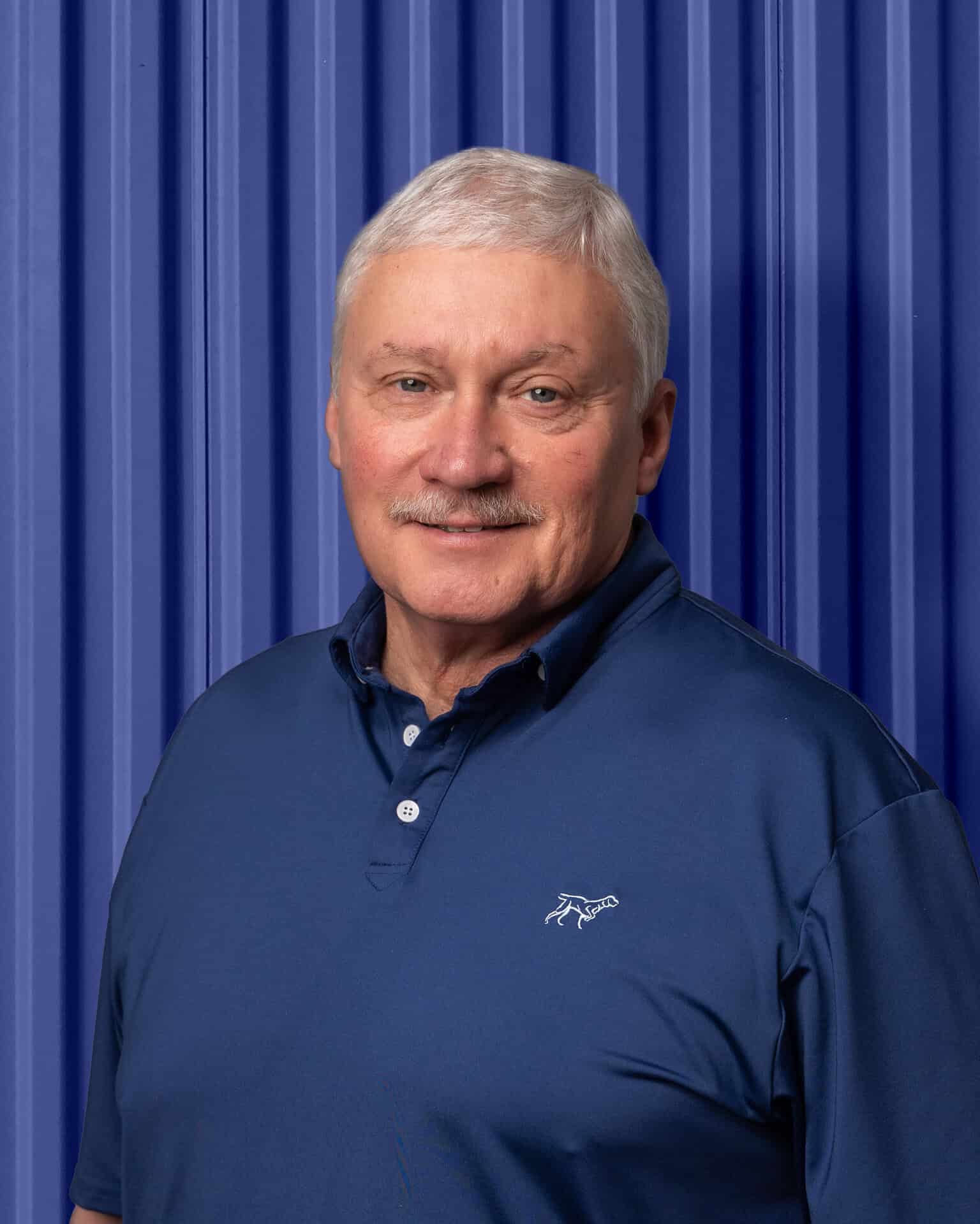 A smiling man in a blue shirt stands against a blue background, embodying Carolina Chem Strip's dedication.