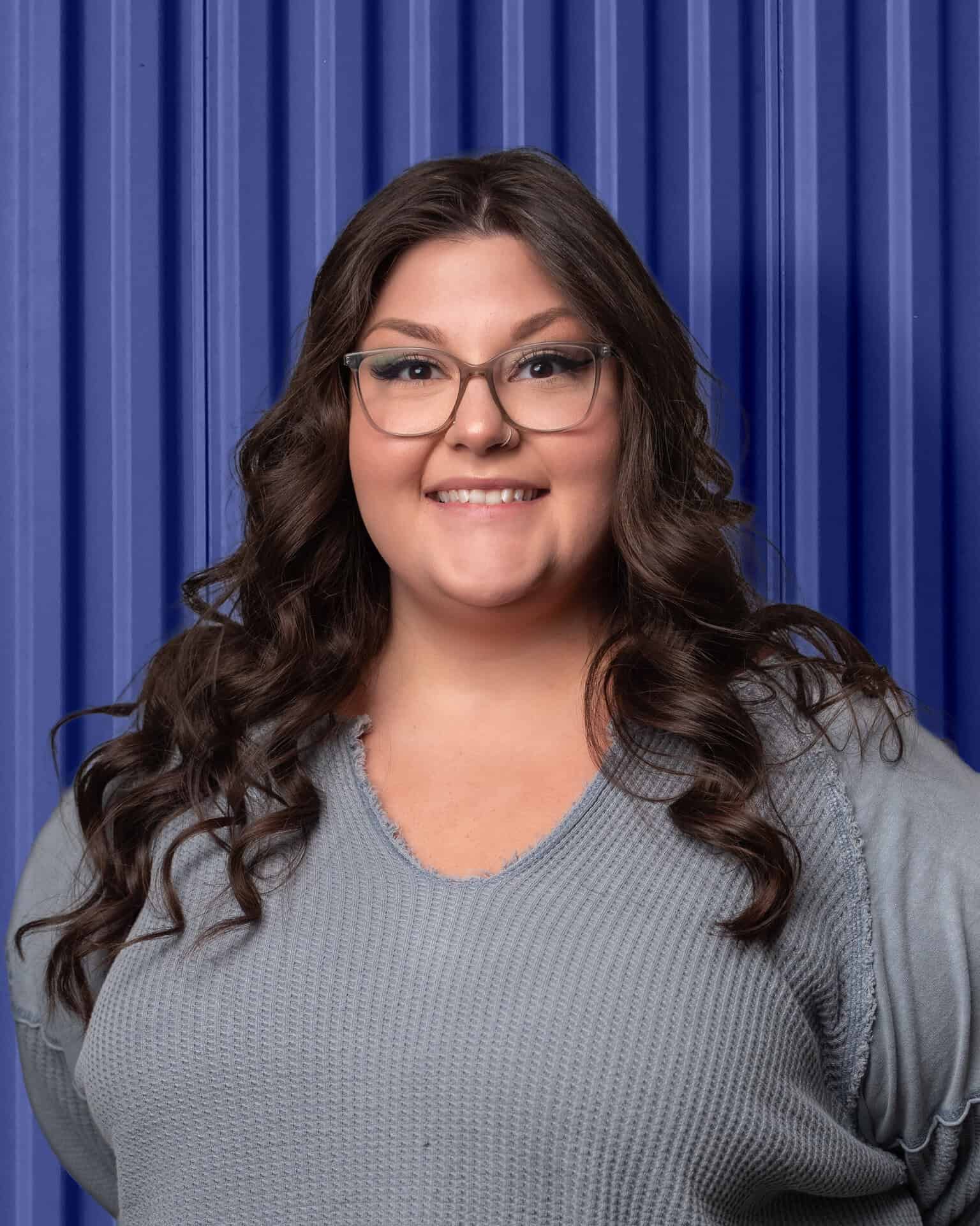 Woman smiling against a blue corrugated background, representing Carolina Chem Strip's dedication to keeping your production moving.