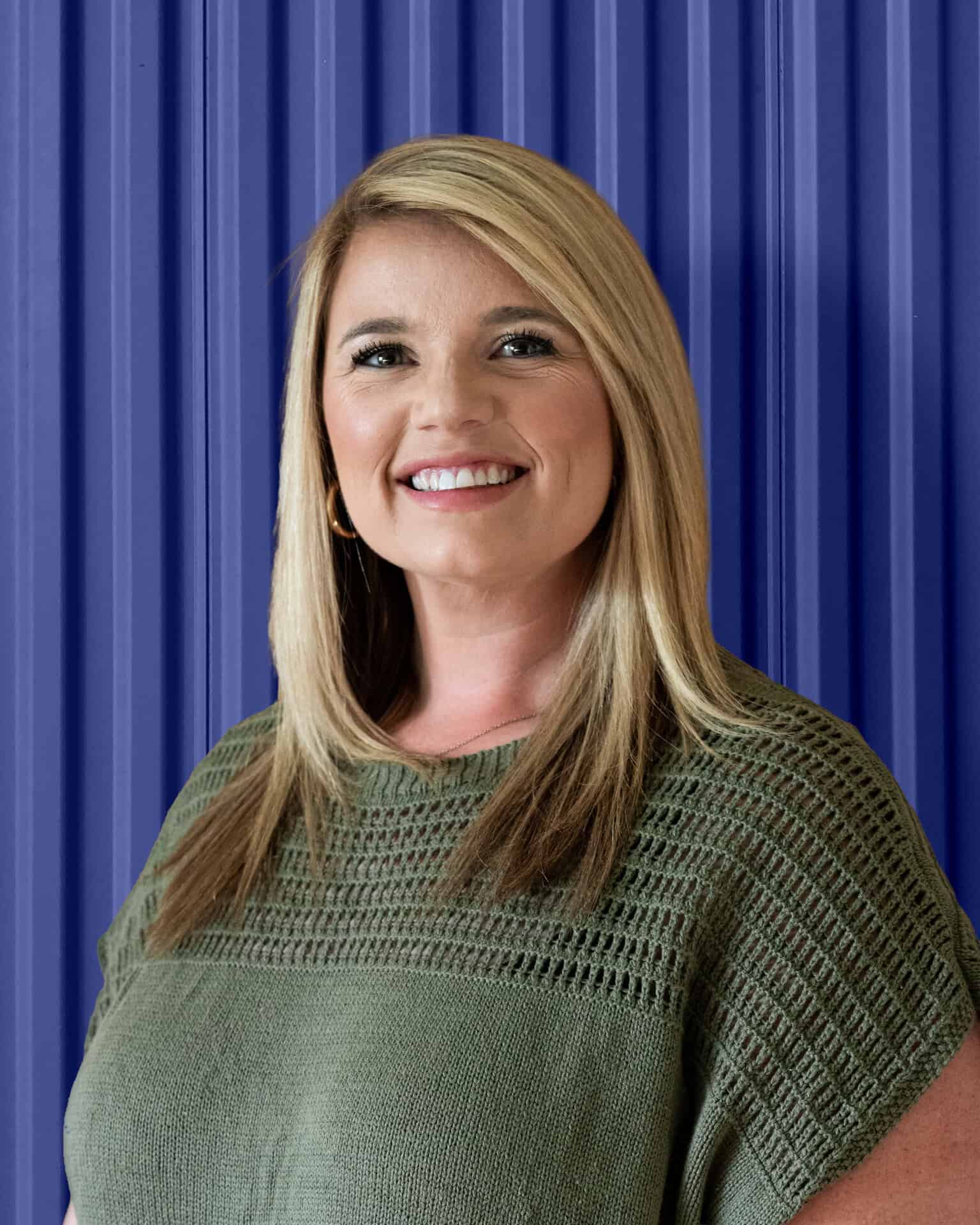 Smiling woman against a blue industrial backdrop, representing Carolina Chem Strip's dedication to helping manufacturers and OEMs keep your production moving.