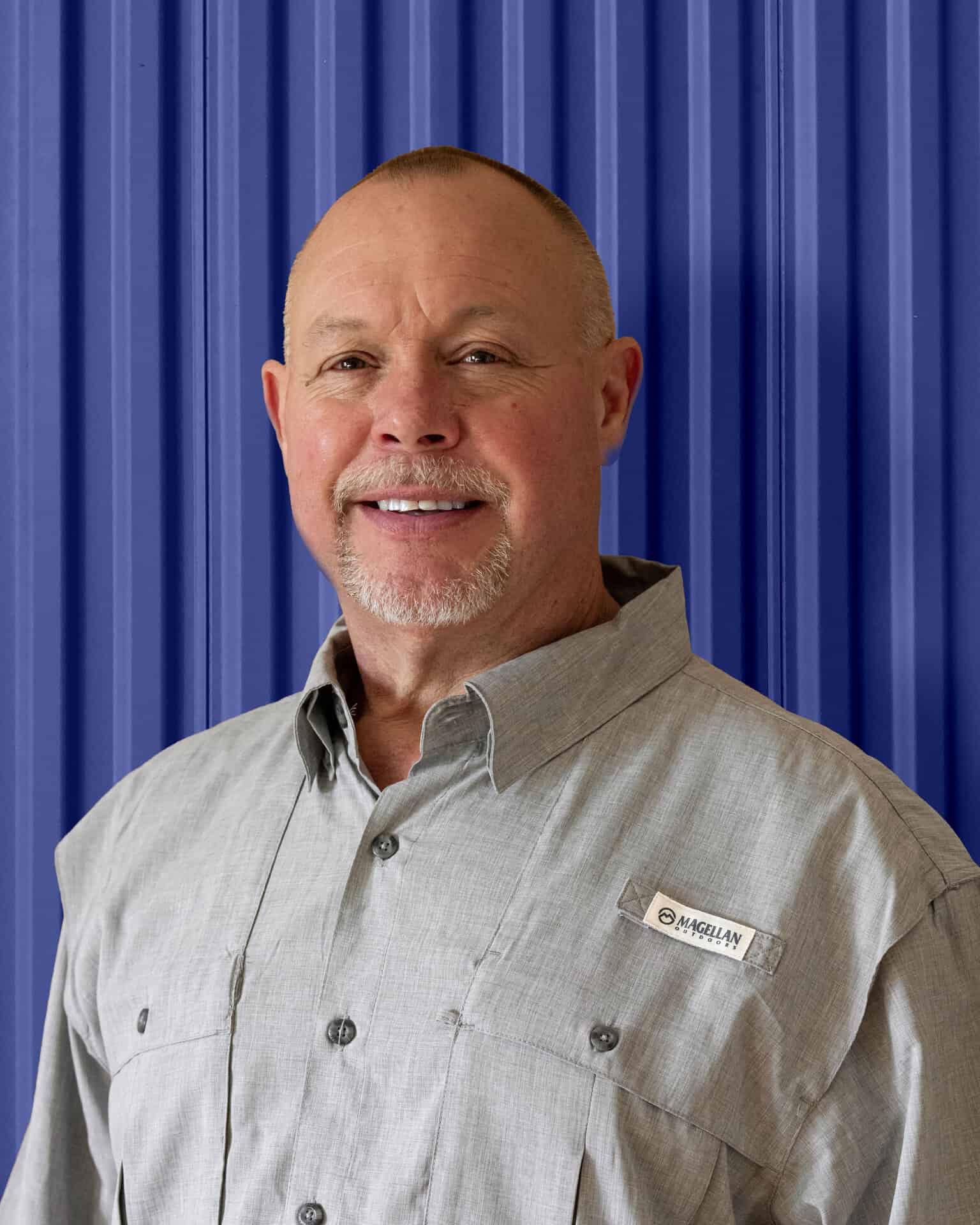 Man in a gray button-up shirt standing against a blue corrugated background, representing Carolina Chem Strip.