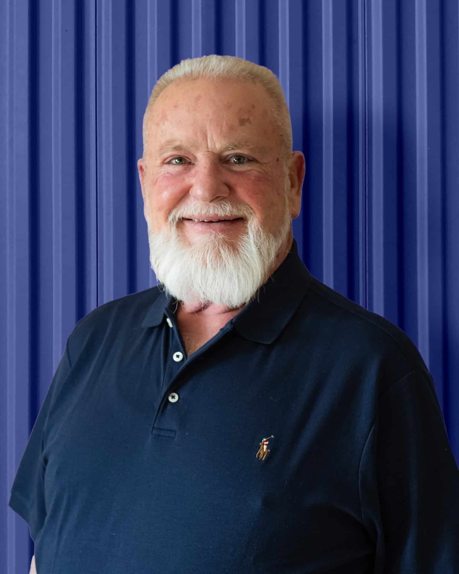 Smiling man in a dark polo shirt against a blue corrugated background, representing Carolina Chem Strip.
