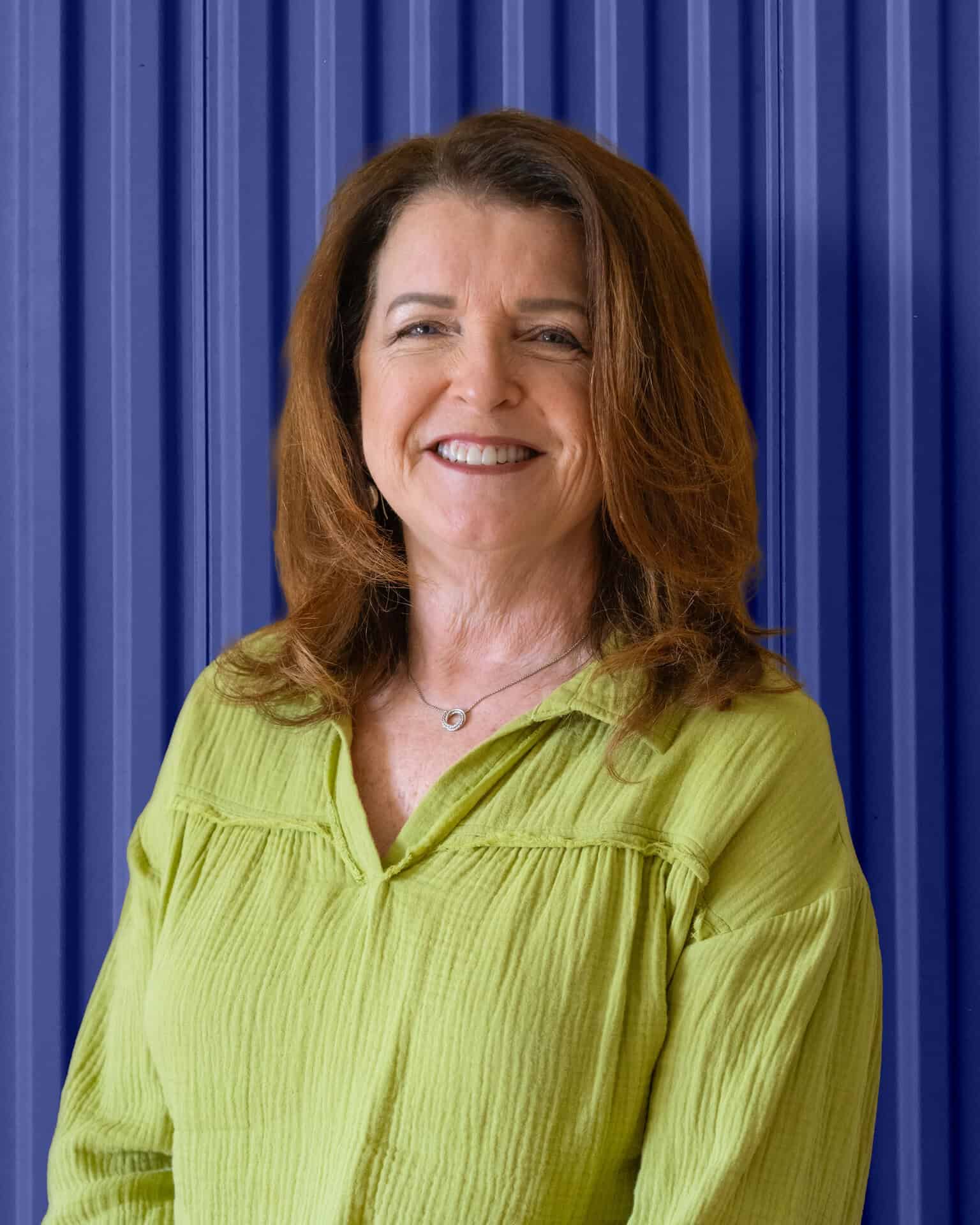 Smiling woman in a green shirt against a blue corrugated backdrop, representing Carolina Chem Strip.