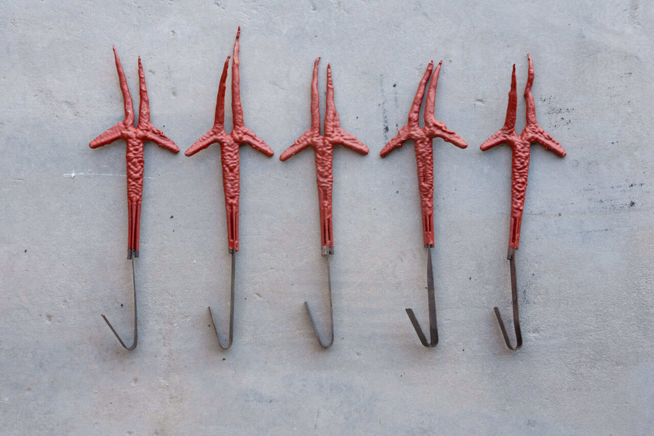 Five metal hooks coated in red paint, used for paint line fixtures, showcasing high-capacity paint removal.